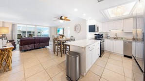 A modern kitchen with white cabinets, a central island, and a dining area with a brown sofa and wooden chairs. - Stunning Sunsets! 2 Bed, 2 Bath Condo on Siesta Key! (Siesta Key)