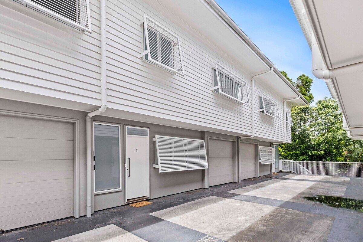 A two-story residential building with white siding, multiple garage doors, and a concrete driveway.
