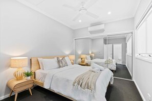 A modern hotel room with a large bed, bedside lamps, a ceiling fan, and a mirror reflecting the room.