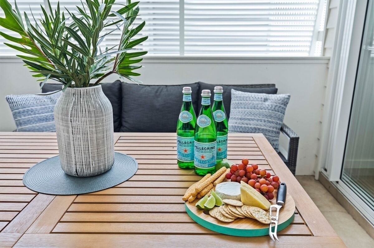 A wooden table with a woven vase, green bottles, a cheese platter, and a knife.
