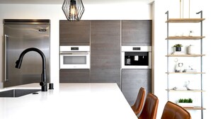 Cocina moderna con refrigerador de acero inoxidable, grifo negro, horno empotrado y estante de madera con adornos.