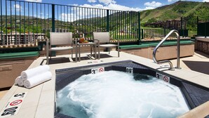 Un jacuzzi con vistas a un paisaje montañoso, rodeado por una cerca y mobiliario de exterior.