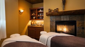 Una habitación con dos camas, una chimenea, un estante con varios objetos y una lámpara fijada a la pared.