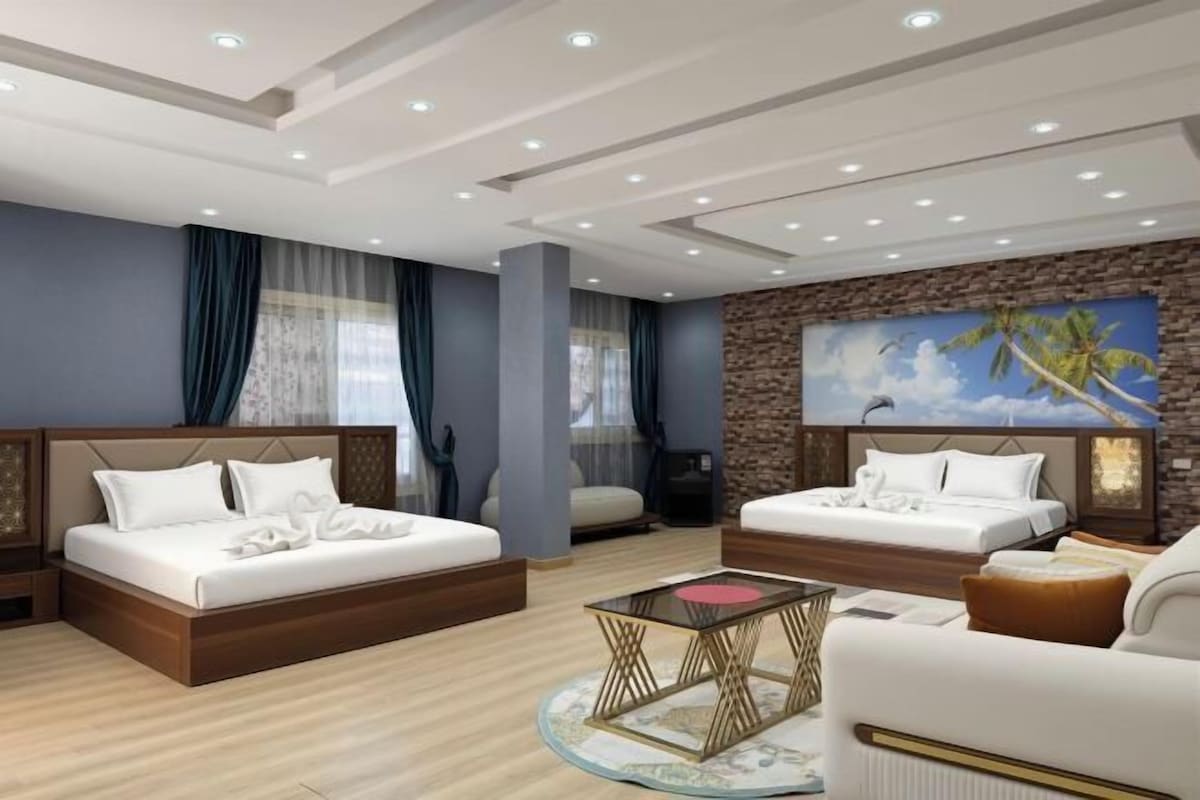 Ein modernes Hotelzimmer mit einem großen Bett, einer Couch, einem Couchtisch und einem Palmenbild.