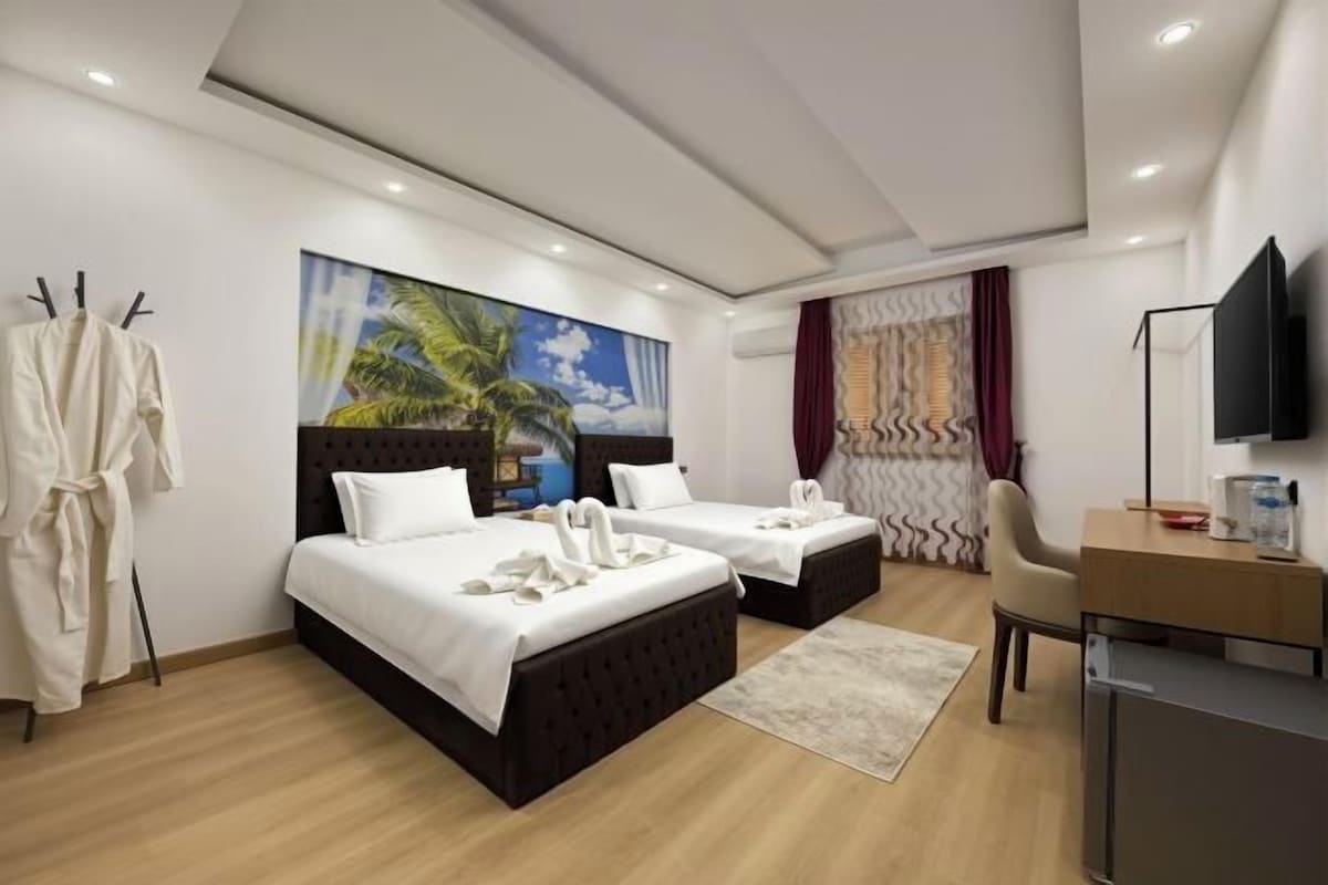 Ein Hotelzimmer mit zwei Betten, einem Schreibtisch, einem Fernseher und einem Bild mit einer Strandansicht.
