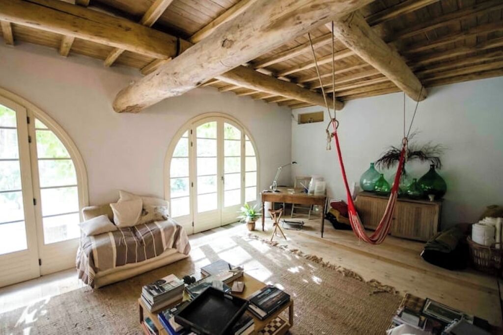 A cozy living room with a wooden ceiling, a sofa, a desk, and a hammock.