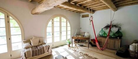 A cozy living room with a wooden ceiling, a sofa, a desk, and a hammock.