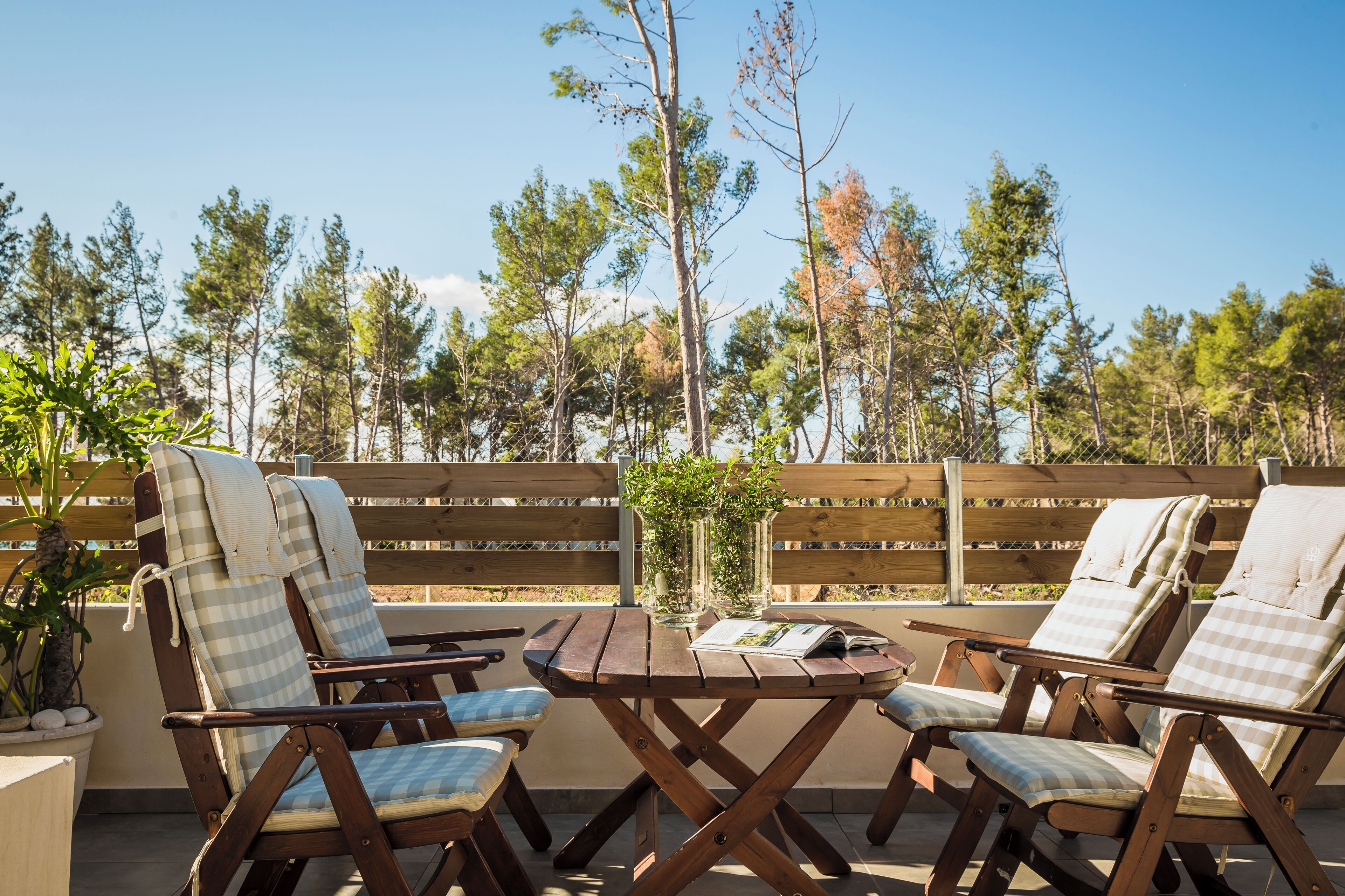 A wooden deck with two checkered lounge chairs and a small table, surrounded by a wooden fence and trees.