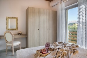 A bedroom with a bed, a wooden wardrobe, a chair, a small table with a tray, and a window with a view of greenery.