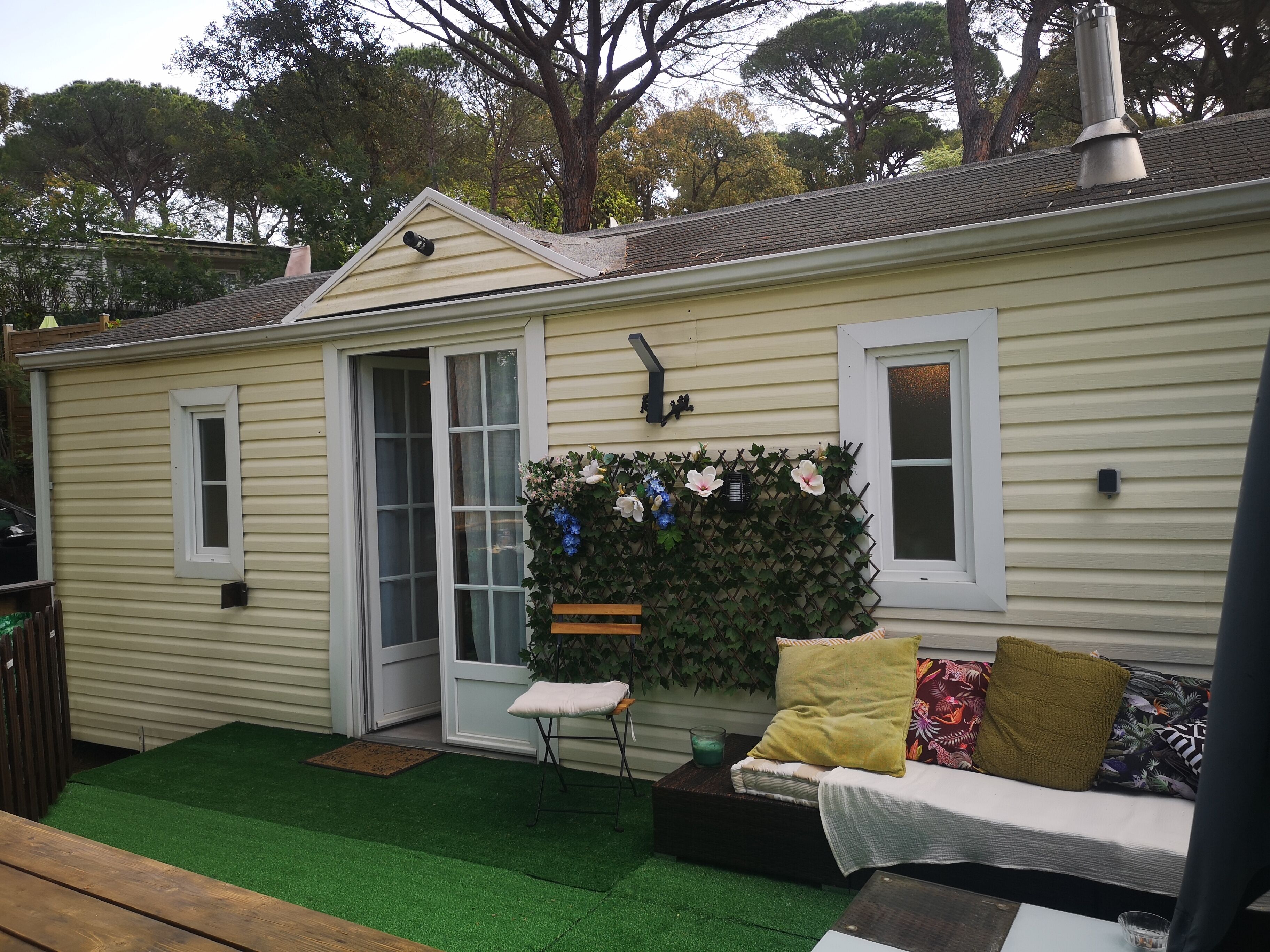 Une petite maison avec une pelouse artificielle verte, un banc et un canapé avec des coussins.