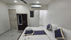 Una habitación de hotel con cama, ventana pequeña, aire acondicionado y puerta.