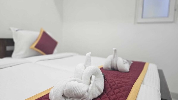 A hotel room with a neatly made bed, a red quilted bedspread, and a white pillow with a yellow trim.