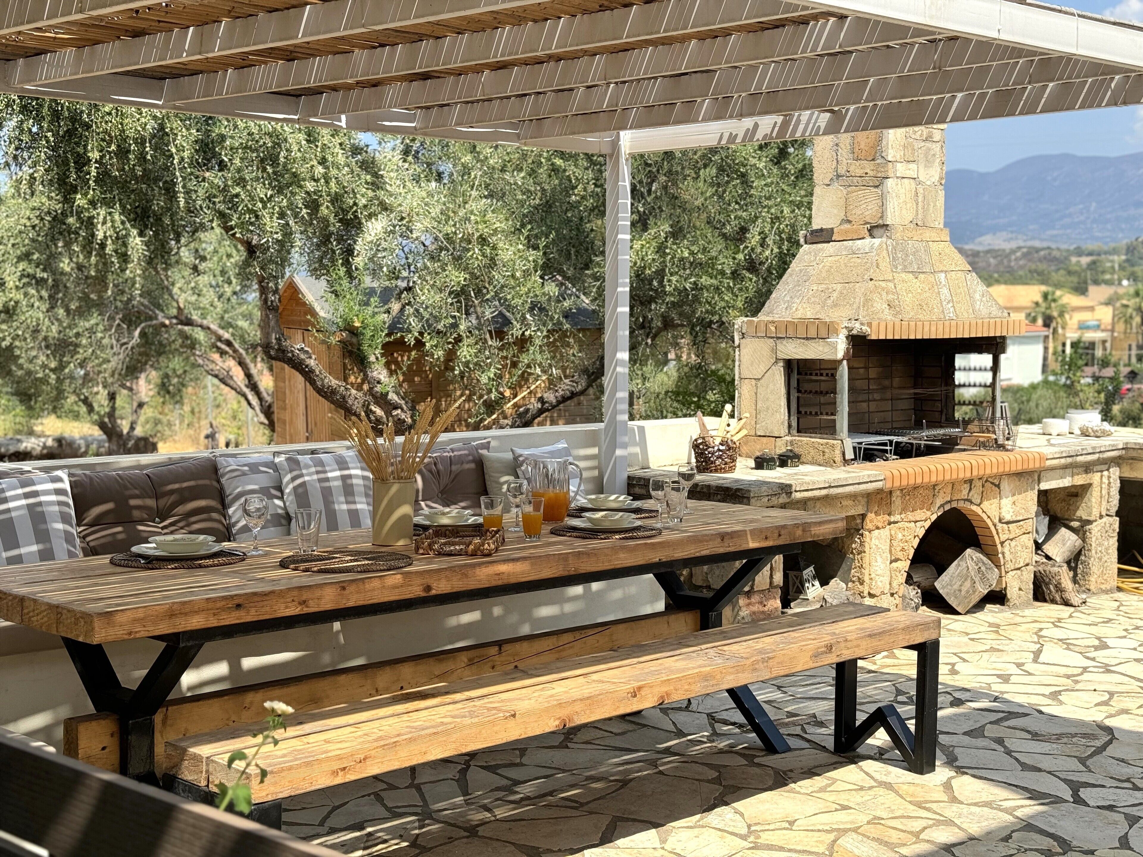 An outdoor dining area with a stone oven, wooden table, and seating.