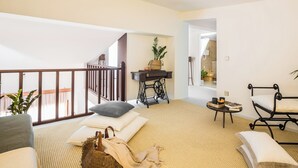Ein großzügiger Wohnbereich mit Sofa, Kissen, einem kleinen Tisch mit Büchern und einer Pflanze, und Blick auf einen Balkon.