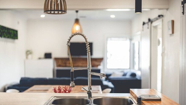 Une cuisine moderne dotée d’un évier en acier inoxydable, d’un robinet au design incurvé original et d’un luminaire suspendu au-dessus.
