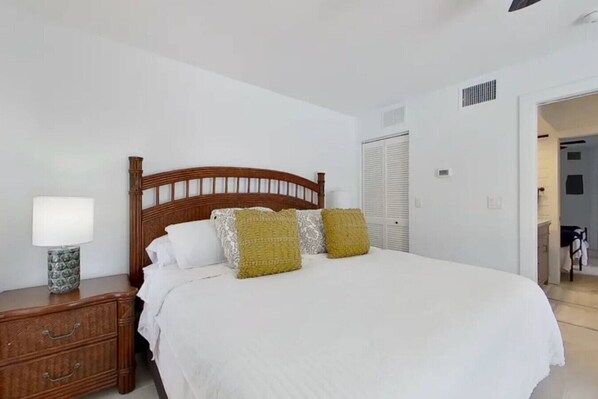 Une chambre à coucher avec un lit en bois, des murs blancs, une table de chevet avec une lampe et une armoire.