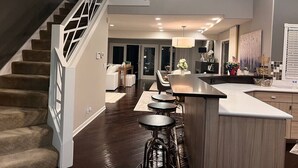Une cuisine moderne dotée d’un îlot central, de tabourets de bar et d’un escalier avec une rampe aux motifs géométriques.