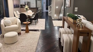 Un salon moderne comprenant un canapé, un fauteuil, un pouf, une table à manger et des chaises. Un escalier mène à un autre niveau.