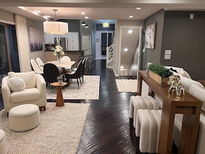 Una sala moderna con sofá, sillón, reposapiés, mesa de comedor y sillas. Una escalera conduce a otro nivel.