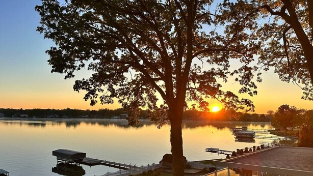 Une vue sur le lac, avec un quai, un arbre et un bâtiment doté d’une terrasse.