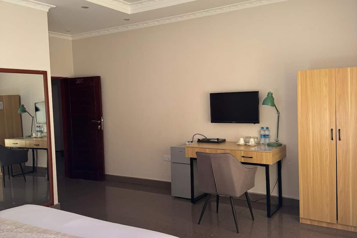 Quarto de hotel com cama, secretária com computador, televisão, guarda-roupa e espelho.