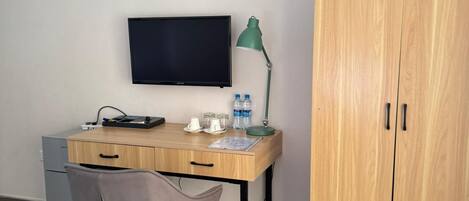 Una habitación con escritorio de madera, una silla, televisor, lámpara, armario y un refrigerador pequeño.