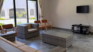 Un salon spacieux, doté de meubles en osier, d’un téléviseur à écran plat et d’un lustre au plafond.