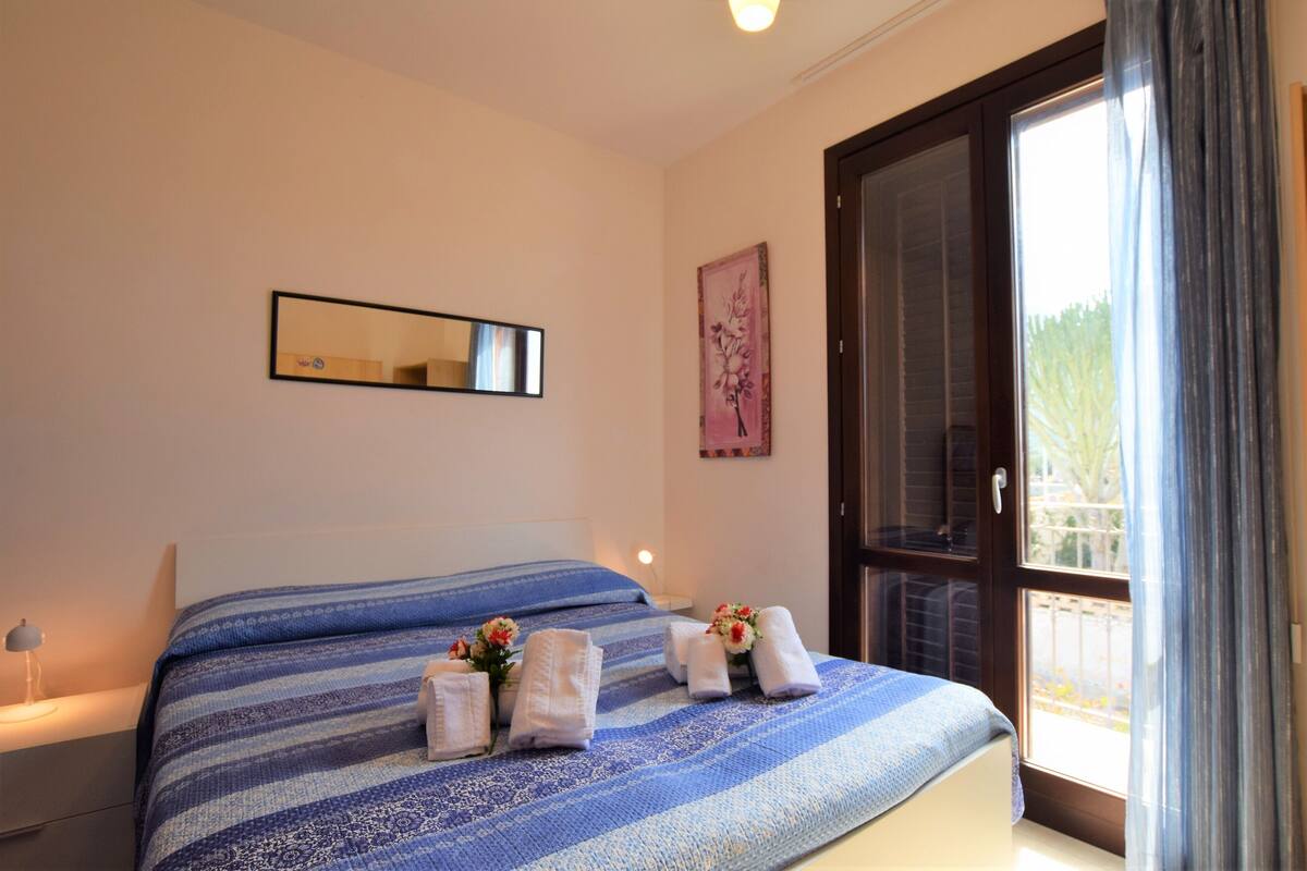 A bedroom with a large bed, a nightstand, a mirror, and a window with curtains.