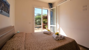 Un dormitorio con una cama grande, una mesita de noche, un equipo de aire acondicionado y vistas al exterior a través de una puerta corrediza de vidrio.