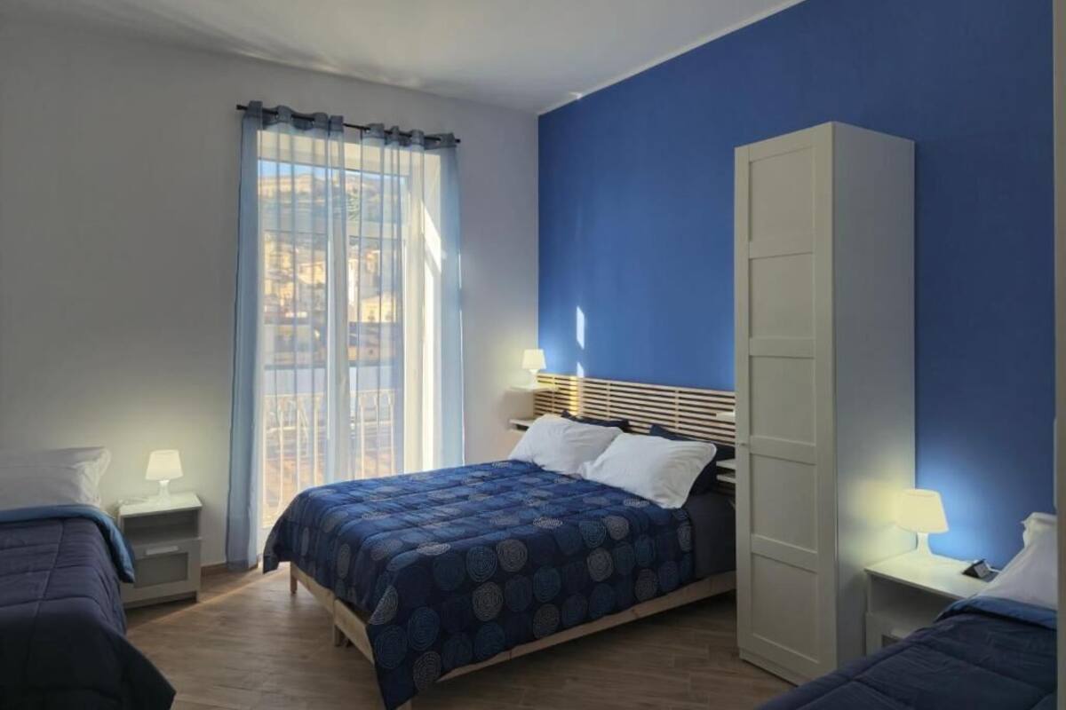 A bedroom with a bed, a wardrobe, a nightstand, and a window with curtains.