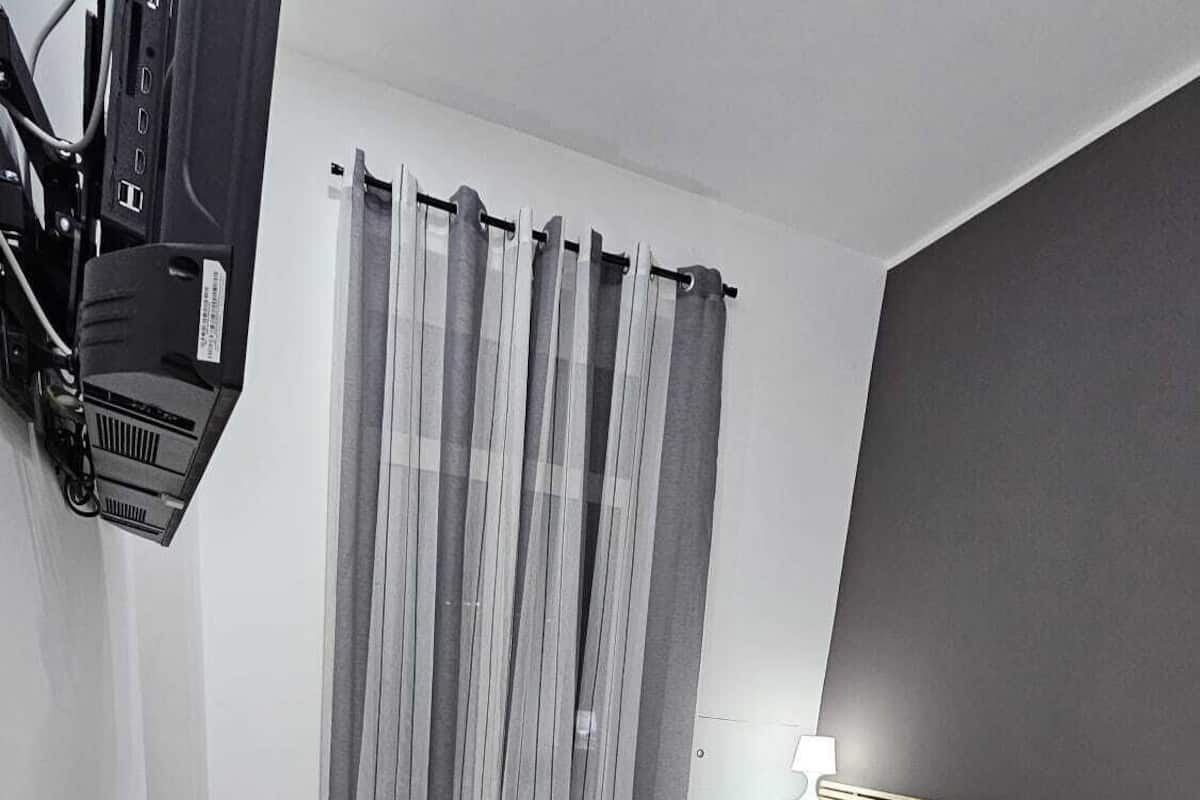 A hotel room with a bed, a desk with a computer, a chair, and a TV mounted on the wall.