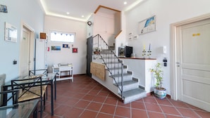 A spacious living area with a staircase, a dining table, chairs, a potted plant, and a kitchen area. - Appartamento Annunziata (Naples)