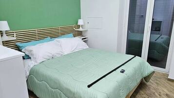 Un dormitorio con cama, mesita de noche, lámpara, armario y puerta corrediza de vidrio que da a un balcón.