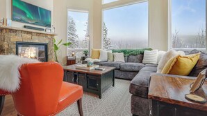 A cozy living room with a fireplace, a large window with a view of snow-covered trees, and a comfortable seating area.