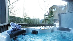 A hot tub with a towel on the edge, surrounded by a wooden deck and a building in the background.