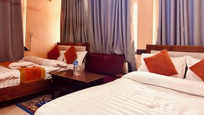 A hotel room with two beds, a small table, a water bottle, and a ceiling fan. - Om Mandakini Hotel (Kathmandu)