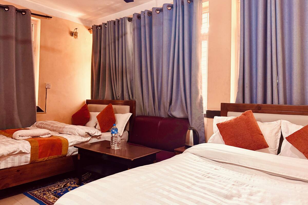 A hotel room with two beds, a small table, a water bottle, and a ceiling fan.