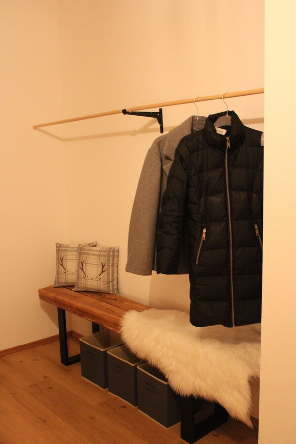 Une pièce comprenant un banc, un porte-manteau avec des vestes et des bacs de rangement.