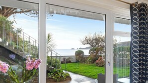 A view through a glass door to a patio area with a grassy lawn, potted plants, and a table and chairs. - 2 Beach Court - Direct Beach Access, Sea Views (Saundersfoot)