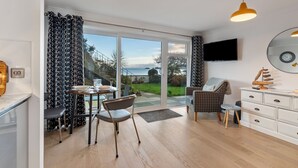 A modern living room with a dining area, a TV mounted on the wall, and a view through the glass door. - 2 Beach Court - Direct Beach Access, Sea Views (Saundersfoot)