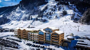 Ein Skizentrum mit mehreren Stockwerken, einer Seilbahn und einem verschneiten Berg im Hintergrund.