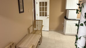 A room with a wooden bench, wicker chairs, a white door, and cabinets. - Marvelous basement apartment with WiFi in Elmont (Elmont)