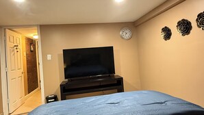 A bedroom with a bed, a TV on a stand, a clock, and decorative wall art. - Marvelous basement apartment with WiFi in Elmont (Elmont)