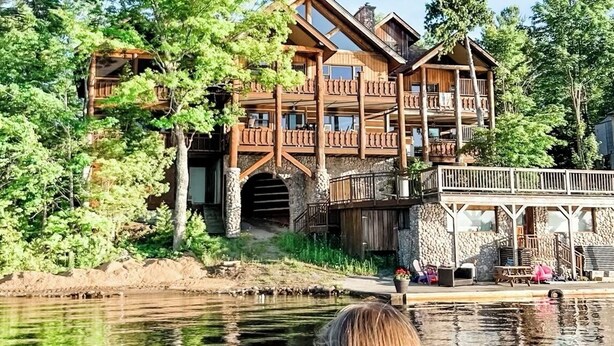 A large wooden lodge with multiple balconies and a stone foundation, situated by a lake. - Fabulous cottage suite, spectacular Stoney Lake view! (Douro-Dummer)