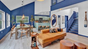 A spacious living area with a large sofa, dining table, and kitchen in the background.
