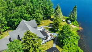An aerial view of a house with a large deck, surrounded by dense greenery and a lake.