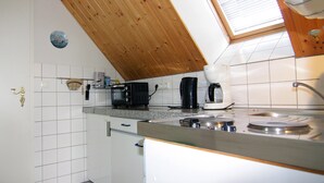 Eine Küche mit weißen Schränken, Holzbalkendecke, einem Fenster mit Jalousien und einer gefliesten Spritzschutzwand.