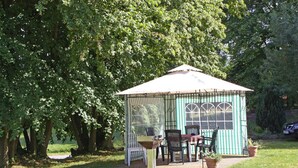 Ein Pavillon mit grün-weiß gestreifter Außenverkleidung, einem Tisch mit Stühlen und Pflanzkübeln.