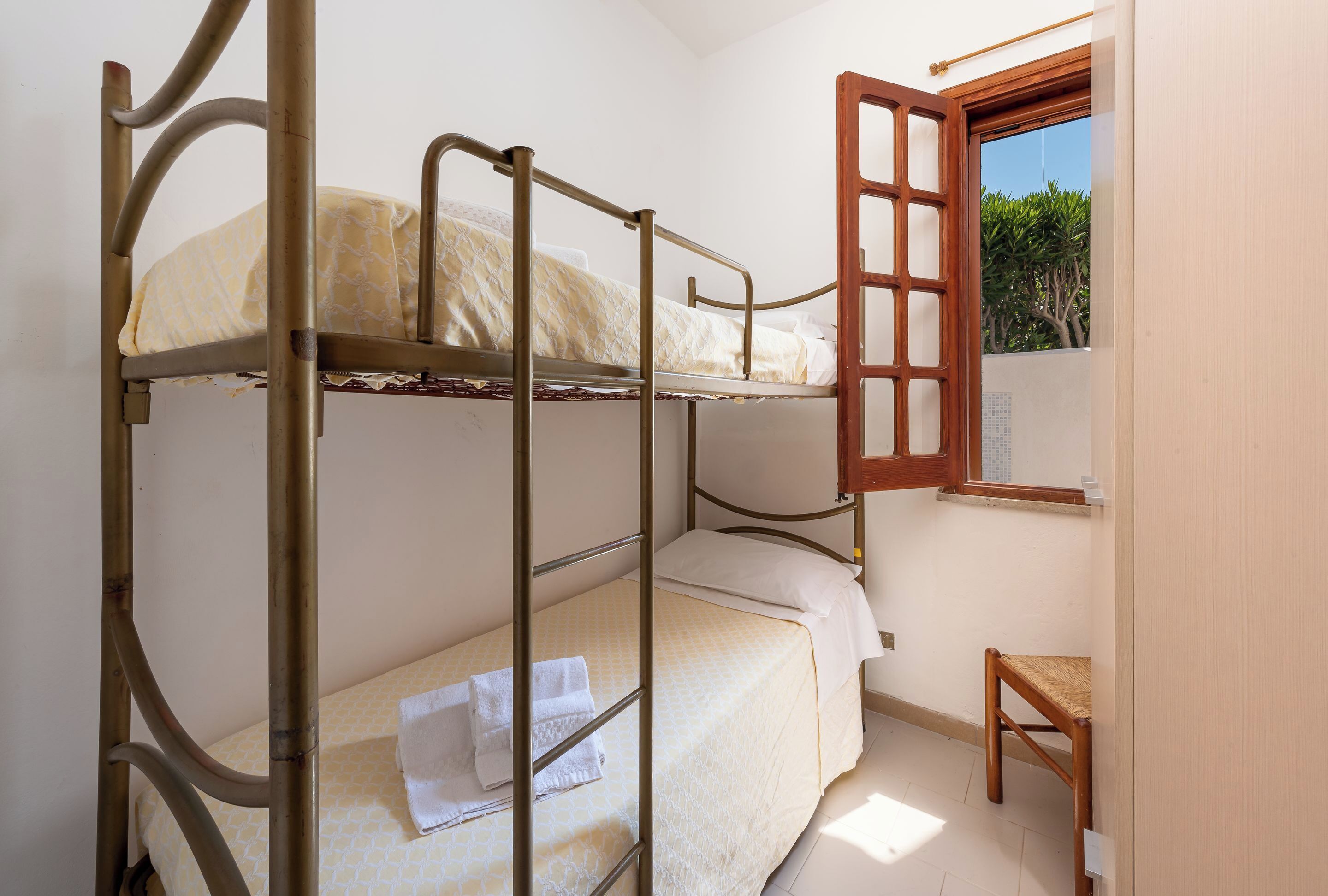 A bunk bed room with a wooden chair and a window with a view of greenery.