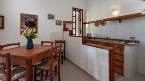 Una cocina con una mesa y sillas de madera, un lavamanos y un jarrón decorativo con flores.